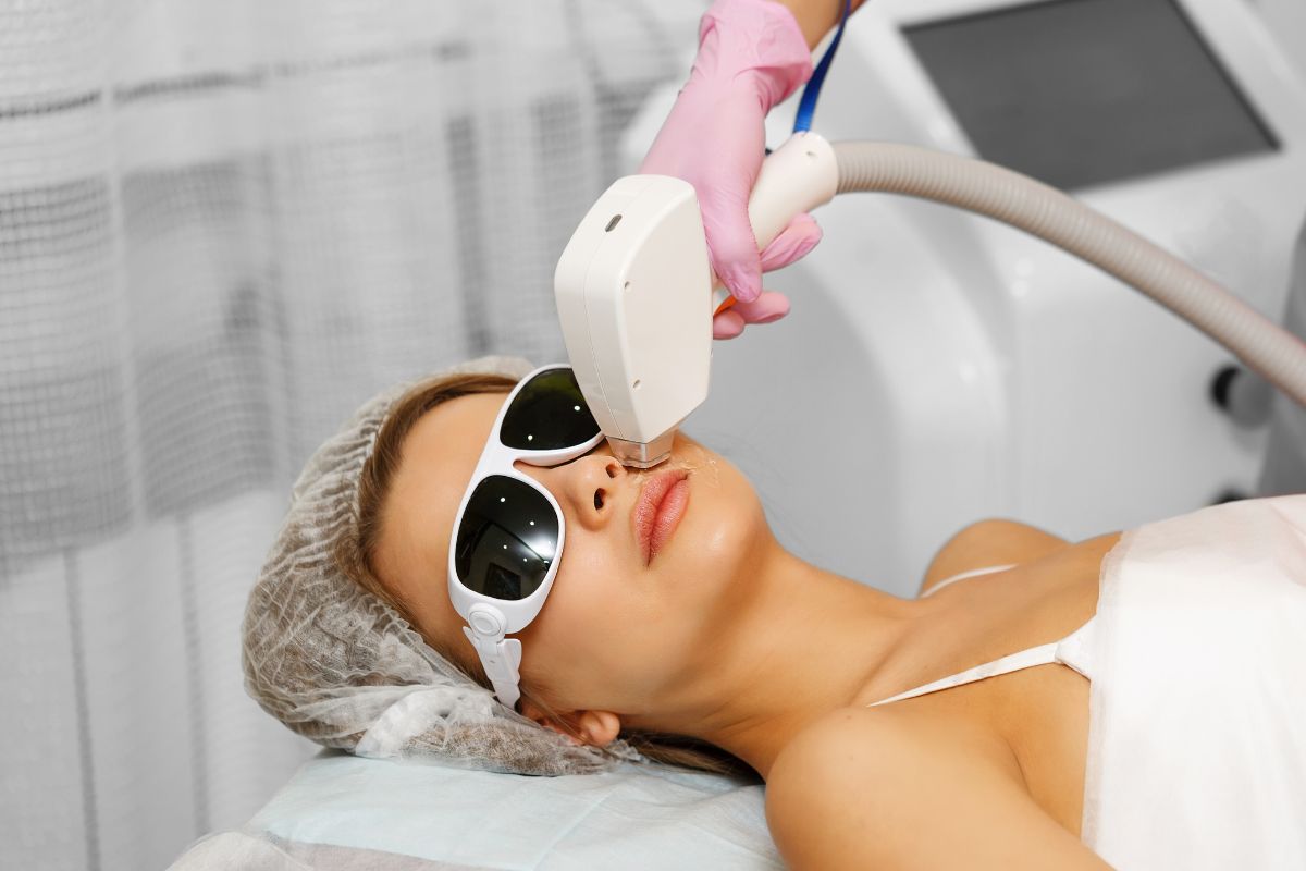 Woman wearing eye protection while a cosmetic physician treats her face using a laser treatment device.