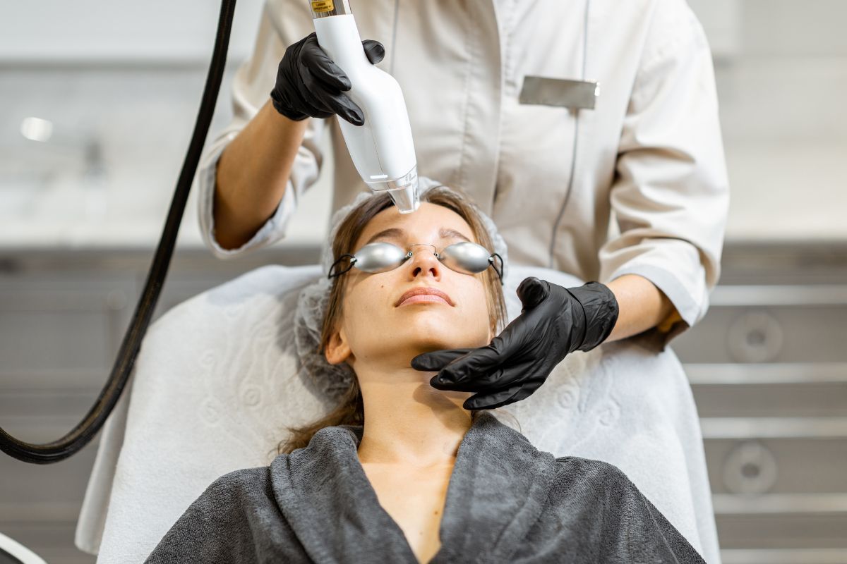Woman wearing eye protection while a cosmetic physician treats her skin using a handheld laser device.